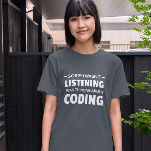 Person wearing a dark gray t-shirt with text 'Sorry I wasn't listening, I was thinking about coding' outdoors.