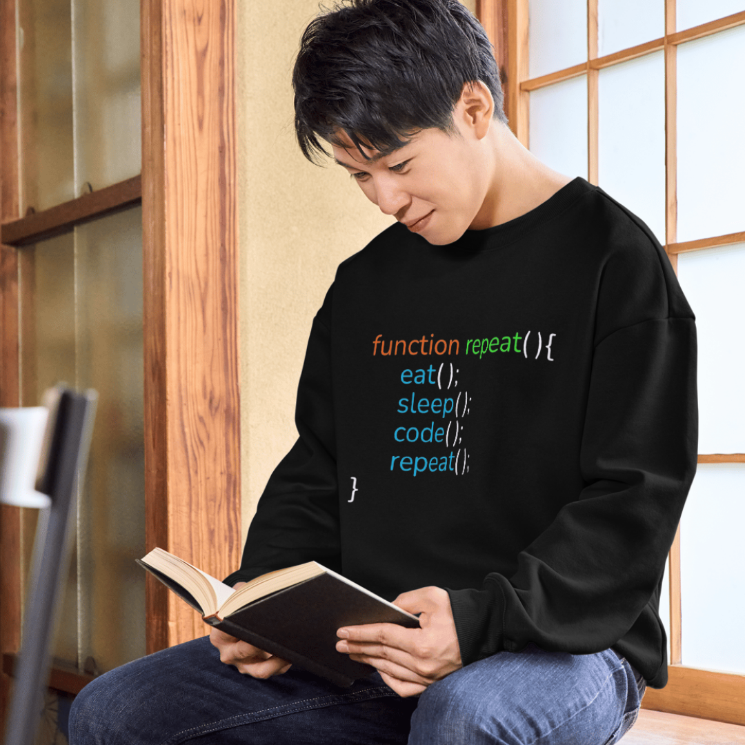 Person wearing a black shirt with colorful coding text, sitting and reading a book.