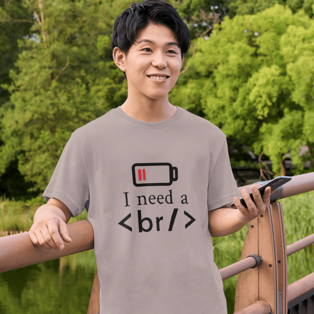 Person wearing a t-shirt with a battery and HTML code design, standing outdoors.