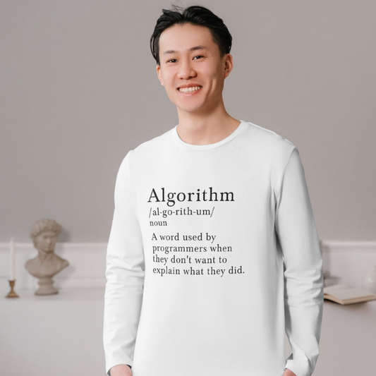 Person wearing a white shirt with a humorous definition of 'algorithm' printed on it, standing in a room with a gray wall and decorative items.