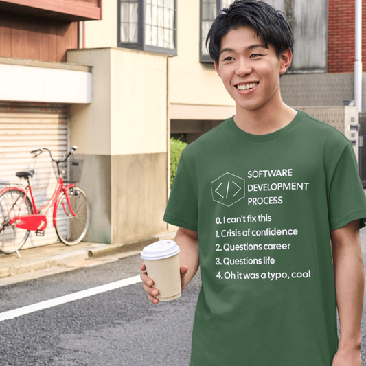Person wearing a green t-shirt with a humorous software development process list, holding a coffee cup on a street.